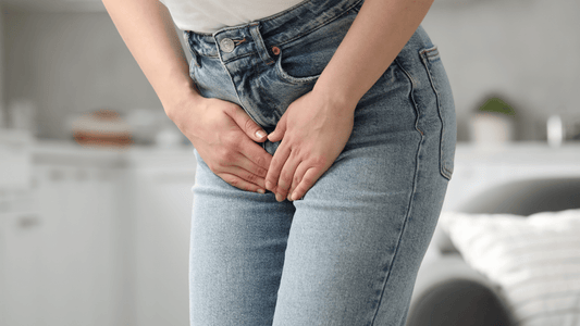 Frau in Jeans, die die Hände an den Schritt hält als müsste sie dringend auf Toilette