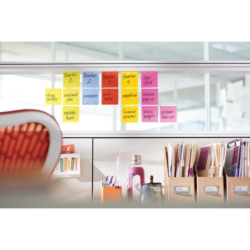 A set of Post-it® Super Sticky Notes (47.6 mm x 47.6 mm, 90 sheets/block, 100% PEFC) from 3M Deutschland GmbH is attached to a glass wall above an office desk with folders, a water bottle, and supplies.
