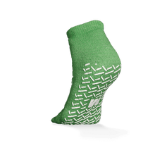 The ECO-PLUS anti-slip disposable socks, double-sided coated by AMPri Handelsgesellschaft mbH, is a green ankle sock with white non-slip grips, depicted on an elevated foot against a white background - ideal for medical areas.