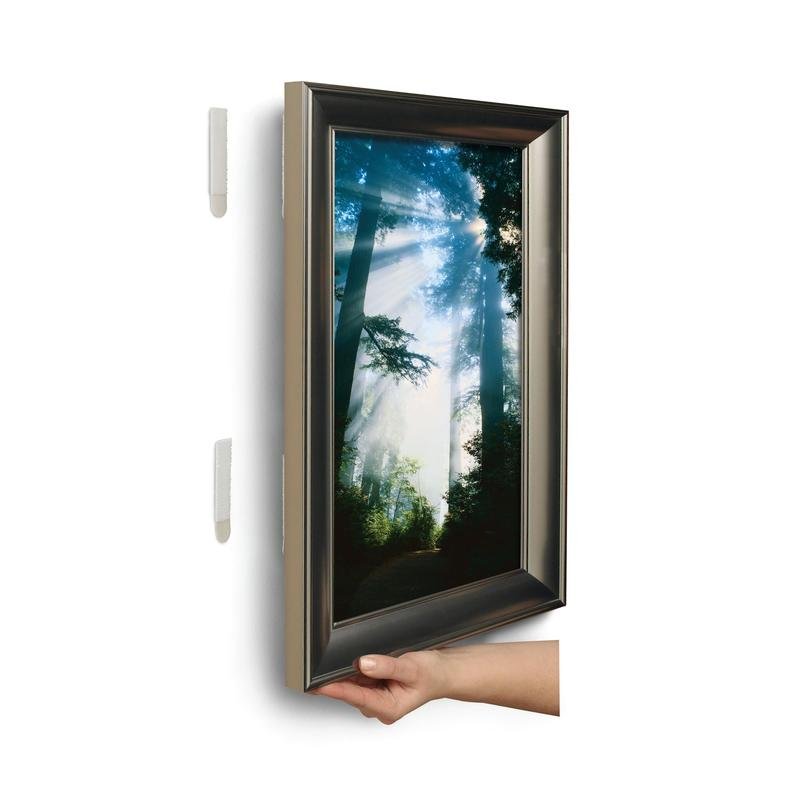 A hand lifts a framed picture from a white wall, revealing two 3M Deutschland GmbH Large Command™ Picture Hanging Strips L, 6 sets in a value pack, behind the picture.
