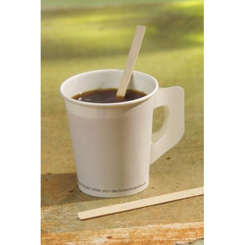 A white paper cup with dark coffee stands on a shelf. A PAPSTAR "pure" stirring stick from PAPSTAR GmbH lies in the cup, another next to it. The background is blurred.