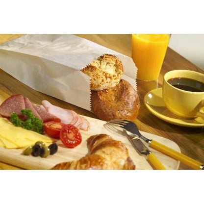 A breakfast spread with cheese, salami, ham, tomatoes, olives, a croissant, rolls in the PAPSTAR 1000 paper folding bag from PAPSTAR GmbH (cellulose), orange juice, and black coffee on a wooden table.