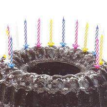 A chocolate cake sprinkled with powdered sugar and decorated with ten PAPSTAR birthday candles 6 cm, color assorted with holder (from PAPSTAR GmbH) in various colors.