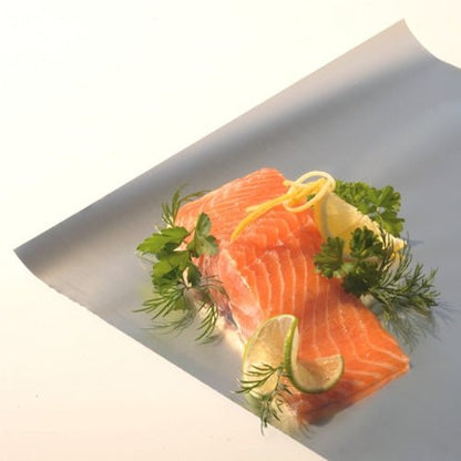 Two raw salmon fillets on Starpak aluminum foil in a folding box, garnished with lemon, lime slices, parsley, and dill. The bright white background highlights the versatile uses of Starpak aluminum foil in the kitchen.