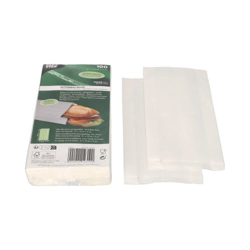 A stack of white PAPSTAR greaseproof sandwich bags (21x10x3 cm) is shown next to the green and white packaging of PAPSTAR GmbH, which shows a sandwich and product information. Next to the package (100 pieces) are some shrink-wrapped bags partially unfolded.