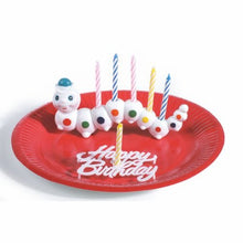A red plate from PAPSTAR GmbH holds a PAPSTAR holder "Würmli" for birthday candles with 6 colorful candles; the caterpillar-shaped holder is adorned with colorful segments and dots.