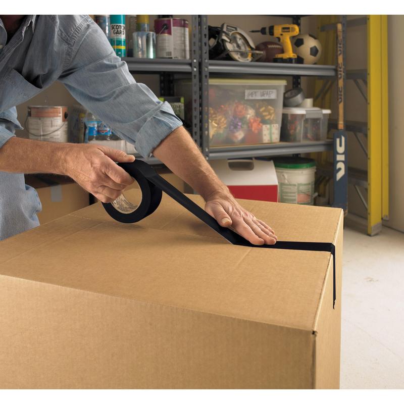 In a garage, a person seals a large box with Scotch® Universal Tape 2904 (50 m x 48 mm) from 3M Deutschland GmbH. On the shelves behind, items like paint cans, a drill, and a soccer ball are stored.