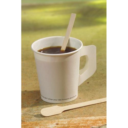 On a surface stands a white paper cup with black coffee, containing a PAPSTAR "pure" stirring stick from PAPSTAR GmbH, with another naturally light stirring stick next to it against a gently blurred background.