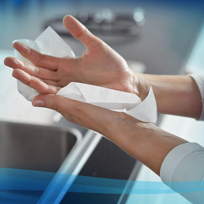 A person dries their hands over a sink in a kitchen with Scott® Essential™ roll towels 6638 Jumbo Roll 1-ply from Kimberly-Clark GmbH; the image is framed with a soft blue border.