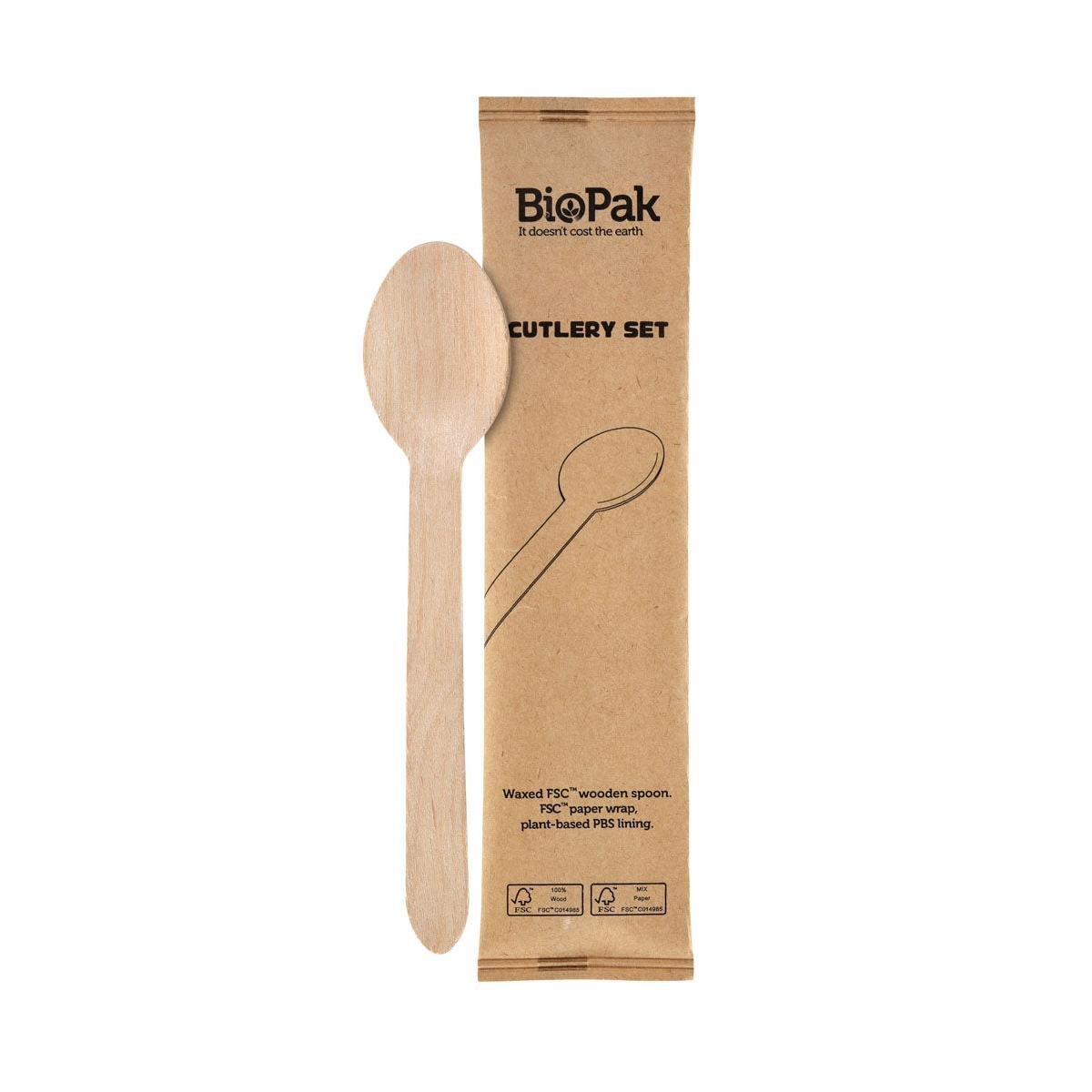 A single wrapped 1/1 spoon Petit made of waxed wood from Duni GmbH lies next to a brown BioPak cutlery set packaging, which indicates sustainable materials and certifications.