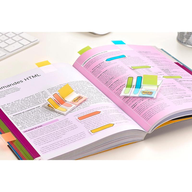 An open book with colored Post-it® Index Strong Filing Tabs, Mini (Blue, Violet, Pink, and Yellow) from 3M Deutschland GmbH marks important HTML sections. A keyboard and a pen holder on a white desk indicate efficient document organization.
