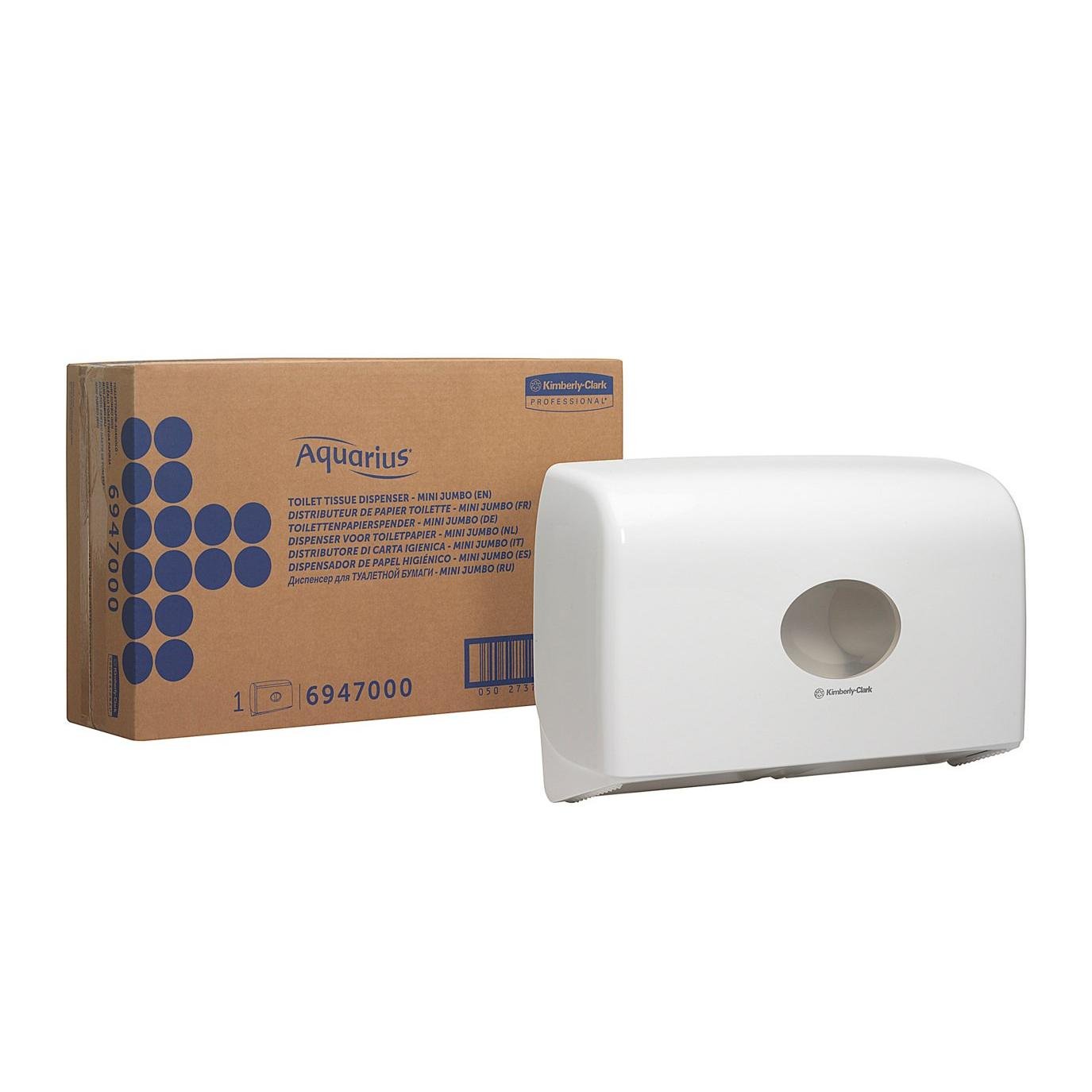 A white Aquarius™ double roll dispenser for Jumbo Toilet Paper Mini by Kimberly-Clark GmbH is mounted on the wall next to a brown box labeled "Aquarius" with blue dot graphics and product information.