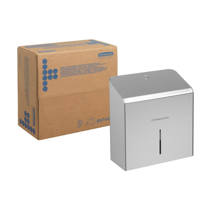 A cardboard box stands next to a Kimberly-Clark Professional™ Mini Jumbo Toilet Paper Dispenser (Stainless Steel) from Kimberly-Clark GmbH, which has a small vertical window on the front.