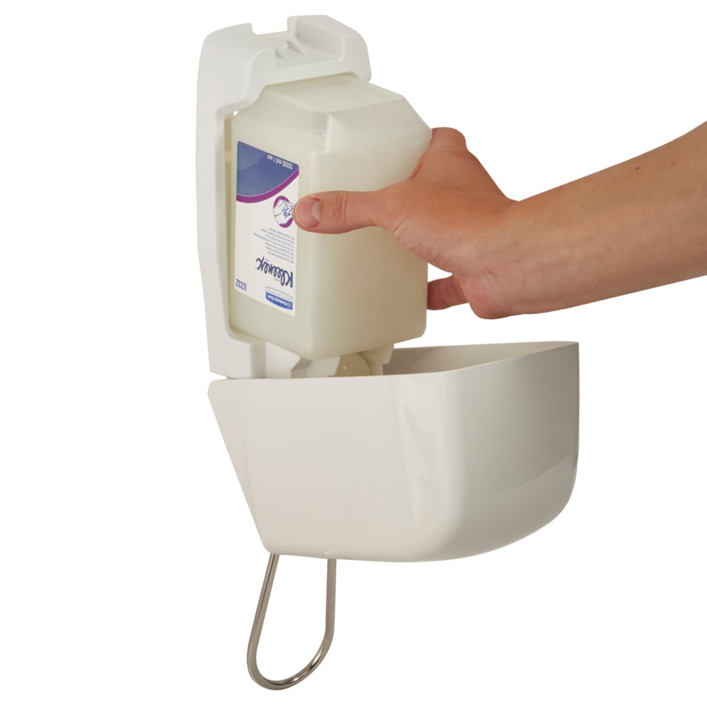 A hand is inserting a 1-liter Aquarius™ hand wash cartridge from Kimberly-Clark GmbH into a white, wall-mounted dispenser with a curved front and a metal support underneath.