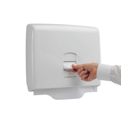 A hand pulls a paper sheet from the white Aquarius™ toilet seat cover dispenser of Kimberly-Clark GmbH, which advertises hygiene in public toilets, against a plain white background.