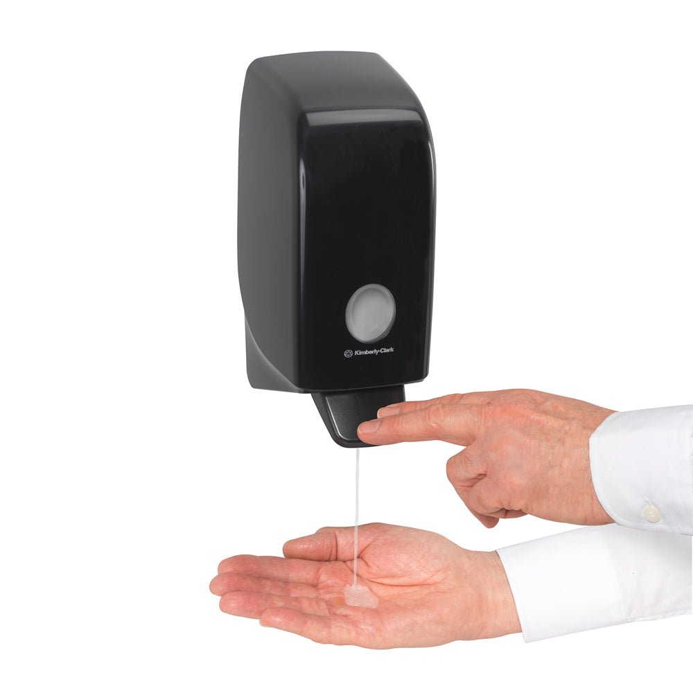 Someone dispenses Kleenex® Hair and Body Shampoo from Kimberly-Clark GmbH from a white 1-liter wall cassette into their palm and presses the lever for effective cleaning and gentle care.