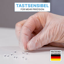 A hand in ARNOMED VINYL PF tactile-sensitive disposable gloves from ARNOWA GmbH grabs a silver ball from several on a white surface. At the top it says: "Tactile-sensitive for more precision." A German flag can be seen at the bottom right.