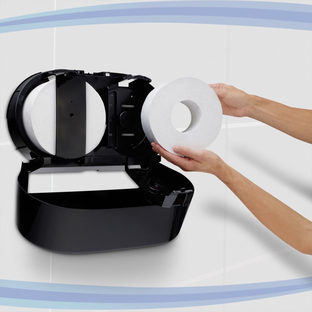 A person loads a jumbo toilet paper roll into a black Kimberly-Clark Professional™ toilet tissue dispenser - center-pull by Kimberly-Clark GmbH, which is mounted on a tiled wall with blue curved lines in the background.