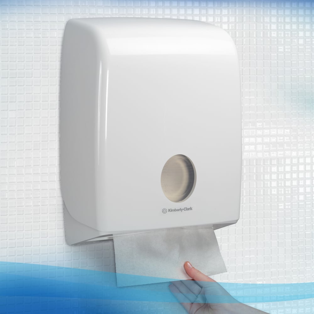 A hand removes an absorbent Scott® CONTROL™ folded hand towel from Kimberly-Clark GmbH from a white wall-mounted dispenser for hygienic hand drying, mounted on a tiled wall.