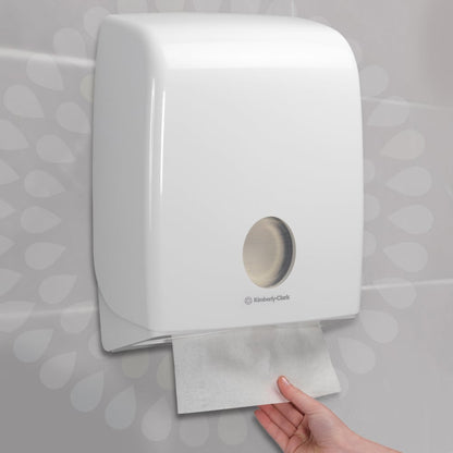 A hand pulls a paper towel from a white, wall-mounted dispenser that ensures hygienic hand drying. Ideal for Kleenex® Ultra™ folded hand towels - Interfold / White (15 clips x 96 sheets), from Kimberly-Clark GmbH.