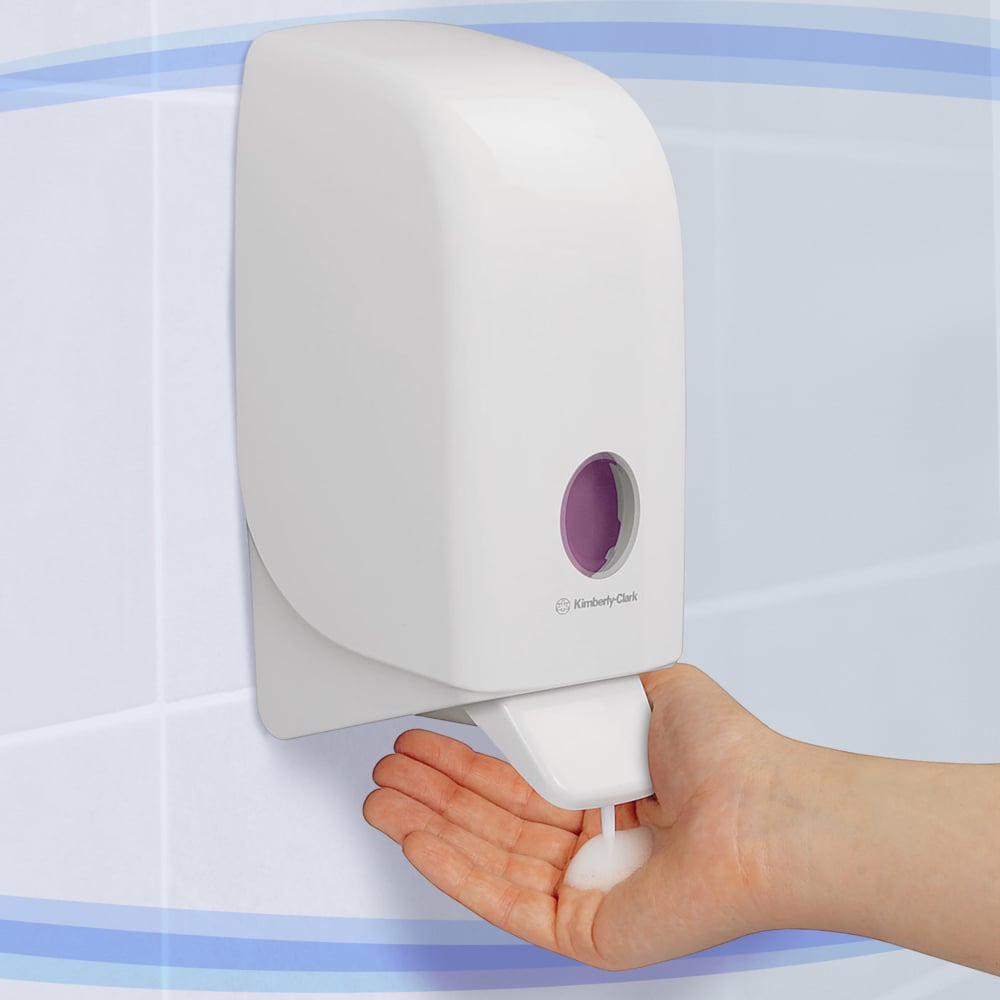 In a tiled bathroom, a person is dispensing foam soap from a white Aquarius™ lotion dispenser—cartridge / 1 Ltr—manufactured by Kimberly-Clark GmbH onto their hand.