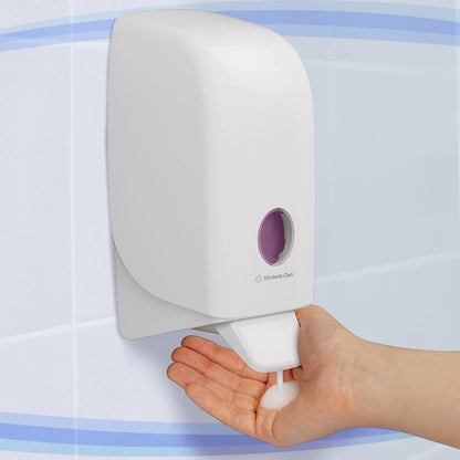 In a tiled bathroom, a person is dispensing foam soap from a white Aquarius™ lotion dispenser—cartridge / 1 Ltr—manufactured by Kimberly-Clark GmbH onto their hand.