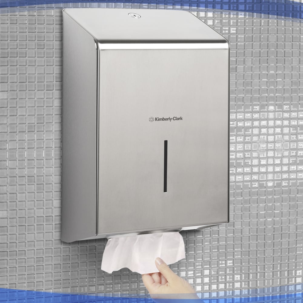 A hand pulls a paper towel from the Kimberly-Clark Professional™ stainless steel towel dispenser (1 dispenser), hygienically mounted on a tiled wall.