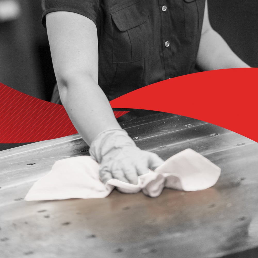 A person in a short-sleeved shirt wipes a large metal surface with a cloth, possibly a Kimberly-Clark GmbH WypAll® X60 General Clean from the BRAG™ Box (41.80 cm x 28.30 cm); the image is mainly black and white with a bold red diagonal in the middle.