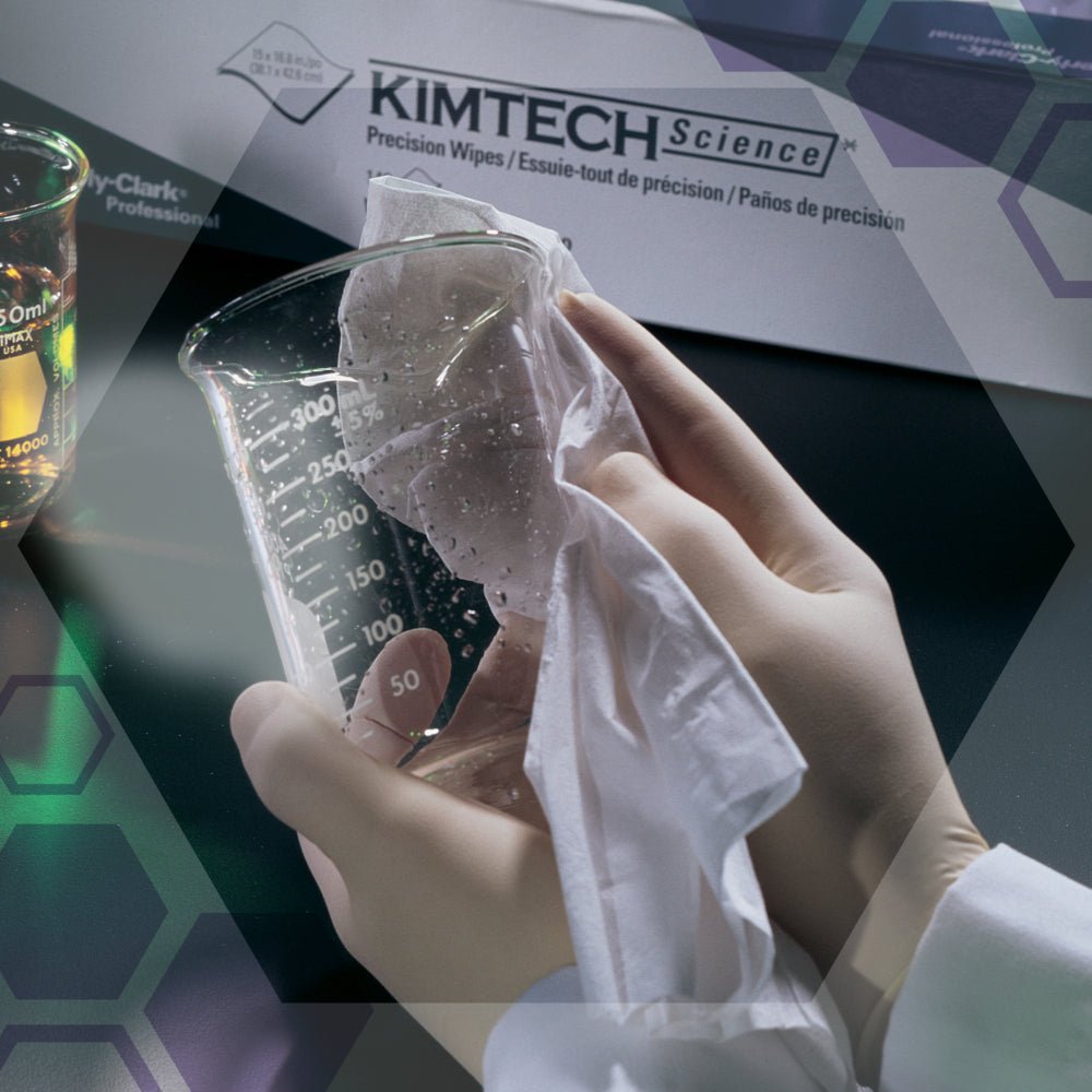 A gloved hand wipes a beaker with a white cloth next to a box of Kimtech® Science Precision Wipes from Kimberly-Clark GmbH (Large, White, 15x196 wipes). Laboratory equipment and other lab wipes can be seen in the background.