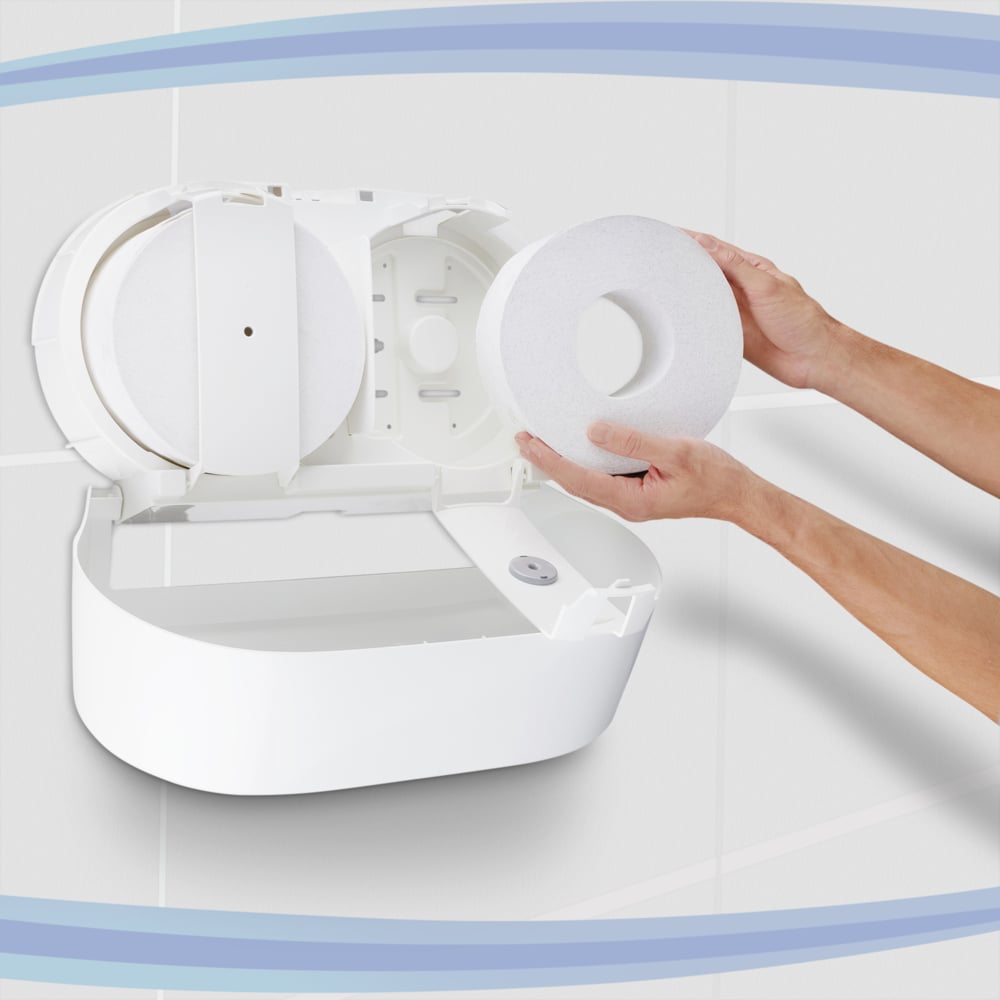 A person inserts a large roll of Scott® Control™ toilet paper - central dispensing from Kimberly-Clark GmbH into a white wall dispenser in a tiled toilet; the opened device releases the compartment and spindle - ideal for professional environments.