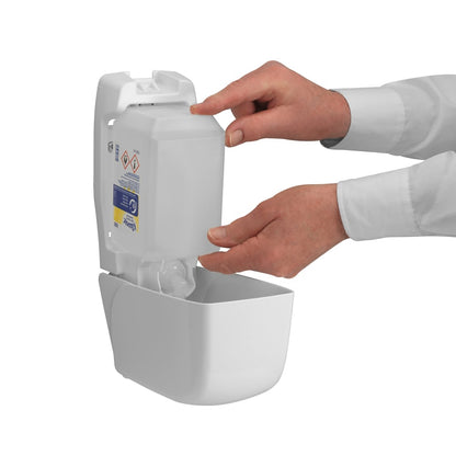 A person refills a wall-mounted Kimberly-Clark GmbH Kleenex® Extra Gel Hand Sanitizer dispenser by inserting a new transparent 1-liter cartridge with both hands; only their hands and forearms are visible through the open front.