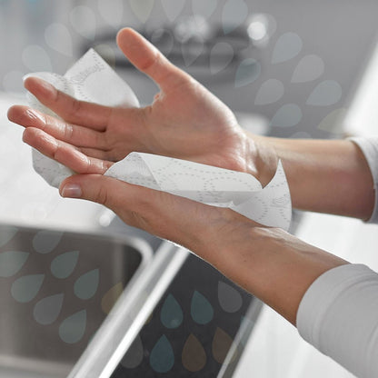 A person dries their hands over a sink with a white 2-ply Kleenex® Ultra™ Roll Towel E-roll Slimroll™ from Kimberly-Clark GmbH. Water droplet shapes overlay the image for a semi-transparent effect.