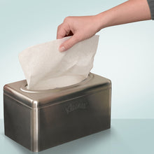 A hand pulls a tissue from a Kimberly-Clark GmbH Kleenex® towel dispenser made of stainless steel - pull-box/small, chrome-plated (2 dispenser boxes/carton), which stands on a light blue surface.