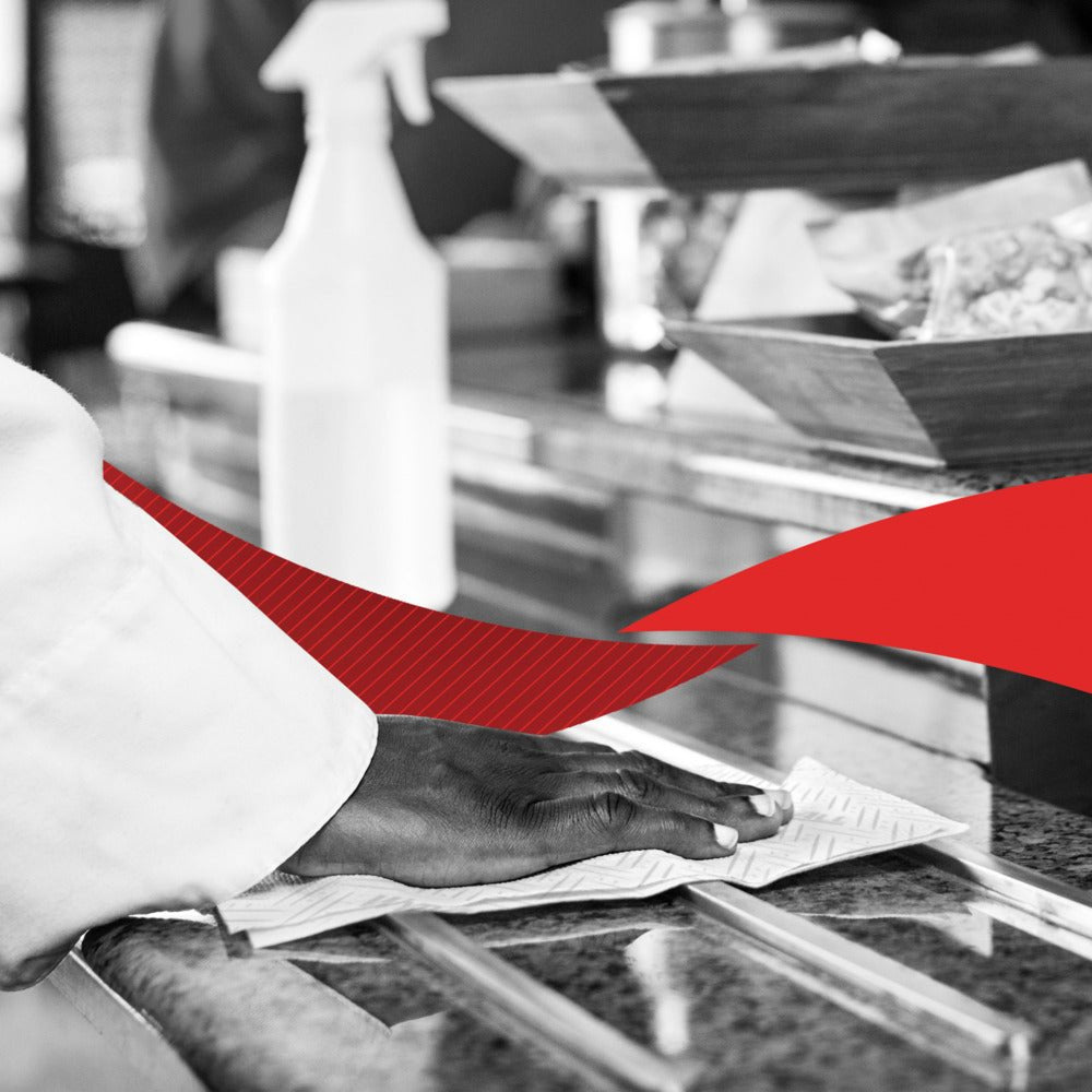 A hand cleans a granite countertop with WypAll® L20 paper wipes (2-ply, 6 x 550 sheets) from Kimberly-Clark GmbH; behind it are a spray bottle and food trays, with a red graphic element across the image.