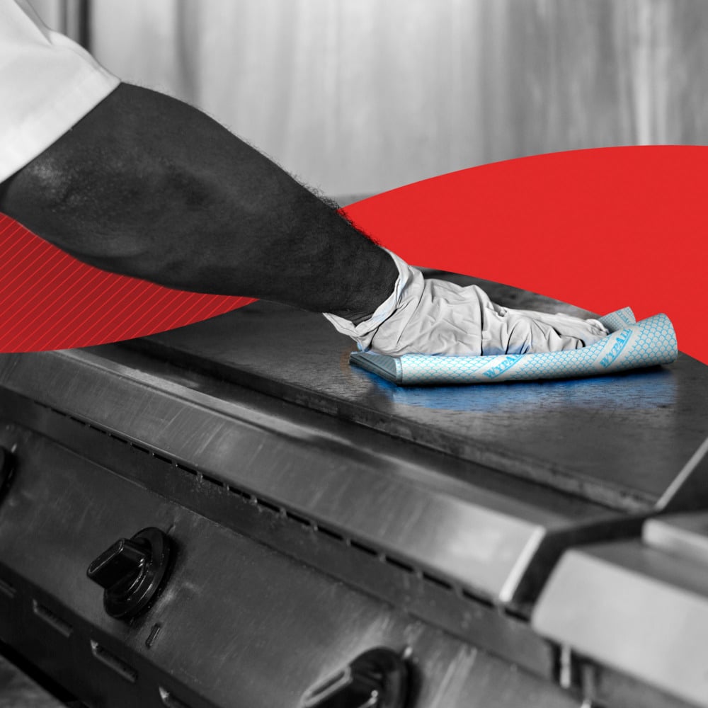 A person with gloves cleans a stainless steel stovetop with a WypAll® X80 Critical Clean - Interfold (41 x 33 cm) cleaning cloth from Kimberly-Clark GmbH. A red graphic highlights its use in industrial cleaning environments.