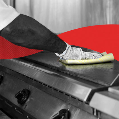A person wipes a commercial kitchen stove with gloves using a yellow WypAll® X80 Critical Clean - Interfold (41 x 33 cm) from Kimberly-Clark GmbH; a red graphic element appears in the background.