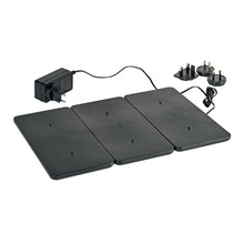 Three black rectangular electronic heating pads are connected to each other next to an LED charging station for lamps (1 piece) from Duni GmbH with multiple sockets and a power adapter on a white background.