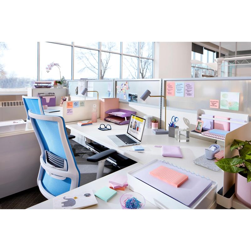 A modern office with white desks, blue chairs, a laptop, plants, and the Post-it® Super Sticky Z-Notes Boost Collection from 3M Deutschland GmbH (76x76 mm, 90 sheets per pad, 100% PEFC). Large windows provide natural light and views of trees.