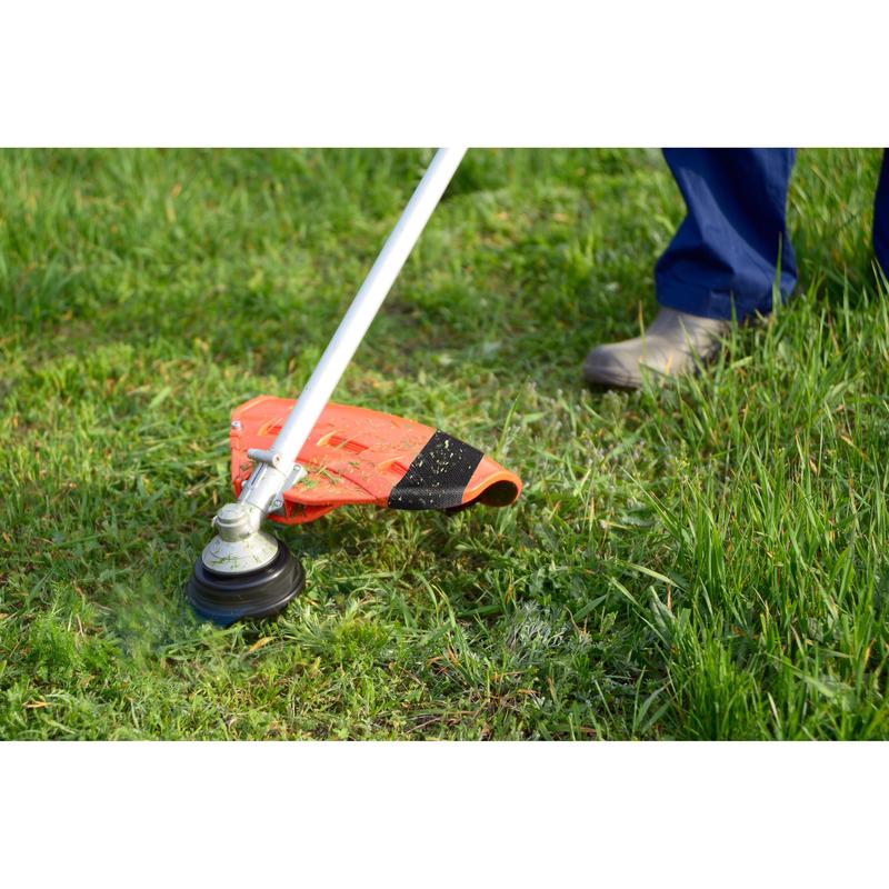 A person in blue pants and boots is trimming uneven green grass outside. Nearby, a roll of Scotch® Extremium™ Ultra High Performance Tape DT17 (25 m x 48 mm, 1 roll) from 3M Deutschland GmbH lies on the ground, ready for strong tape requirements.