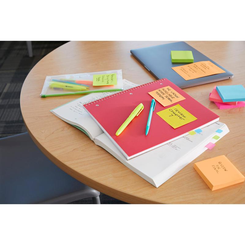 A round wooden table is shown with a red notebook, an open textbook, pens, highlighters, a laptop, a clear plastic sleeve, and 3M Deutschland GmbH Post-it® Super Sticky Z-Notes (Boost Collection, 76x76mm); a chair is partially visible.