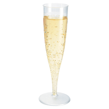 A tall, slender champagne glass packaged in a box, 135 ml Transparent by Duni GmbH, filled to the brim with sparkling champagne, whose visible bubbles gracefully rise to the surface. The glass stands elegantly against a simple white background, making it perfect for upscale events.