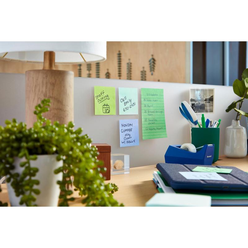 A tidy office desk with a 3M Post-it® Super Sticky Notes block (76 x 76 mm, 90 sheets, 100% PEFC) from Deutschland GmbH with handwritten reminders on the partition, along with a lamp, a plant, stationery, notebooks, and a photo pinned to the partition.