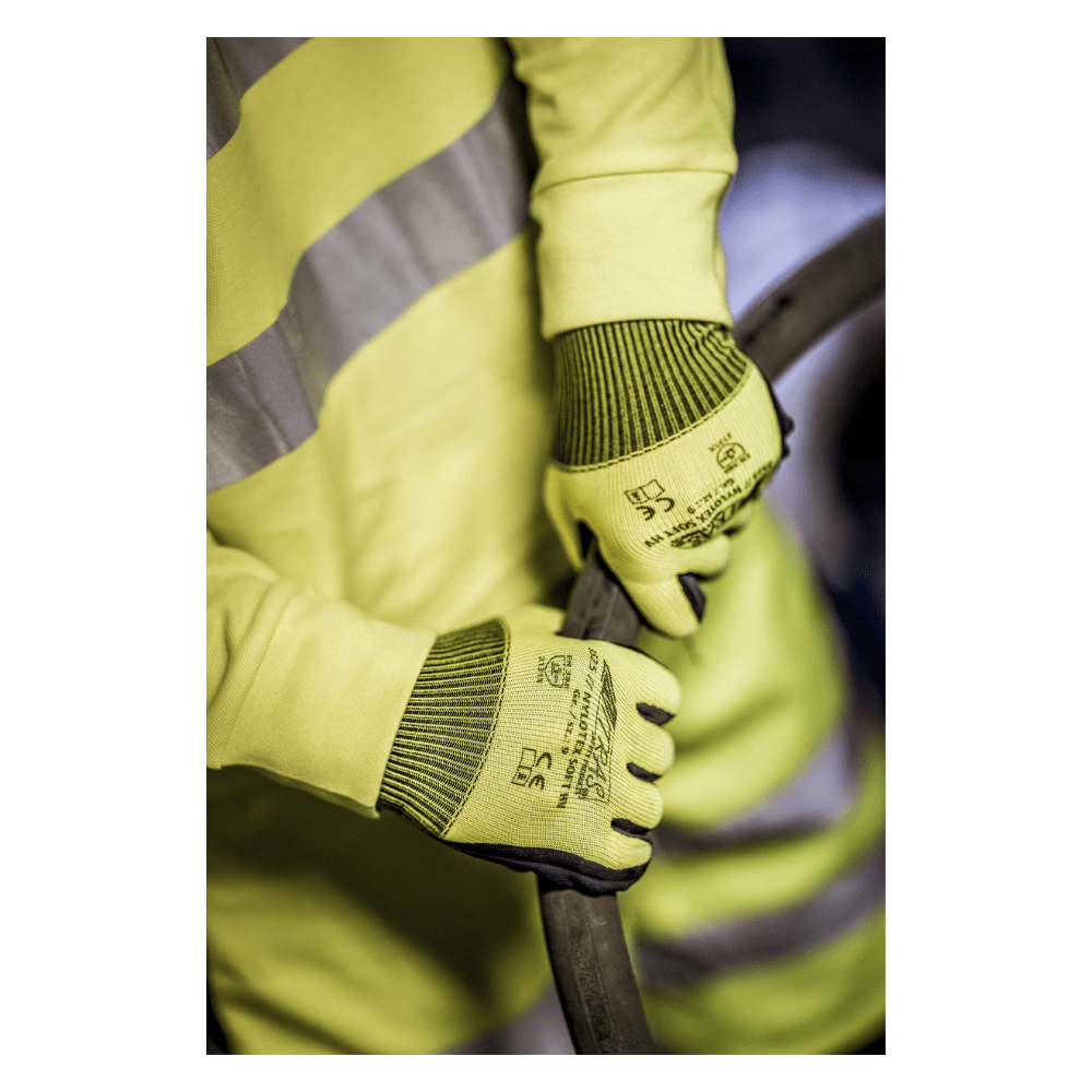 A person wearing a yellow safety vest and NITRAS NYLOTEX SOFT HV nylon gloves from AS Arbeitsschutz GmbH, neon yellow, partially coated – with black text and safety symbols – is holding a thick, dark cable or hose.