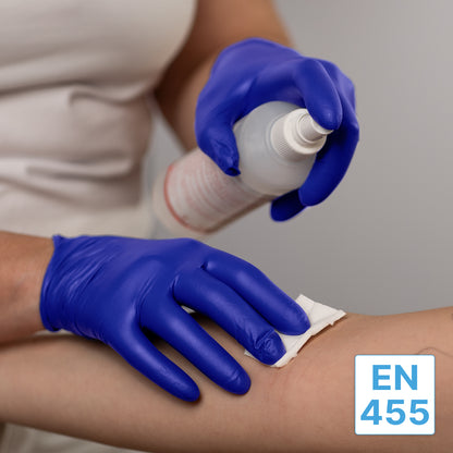 A person wearing ARNOMED NITRIL XTRA PURE disposable nitrile gloves from ARNOWA GmbH is cleaning another's arm with a white cloth and a spray bottle. The label "EN 455" appears in the lower right corner of the image.