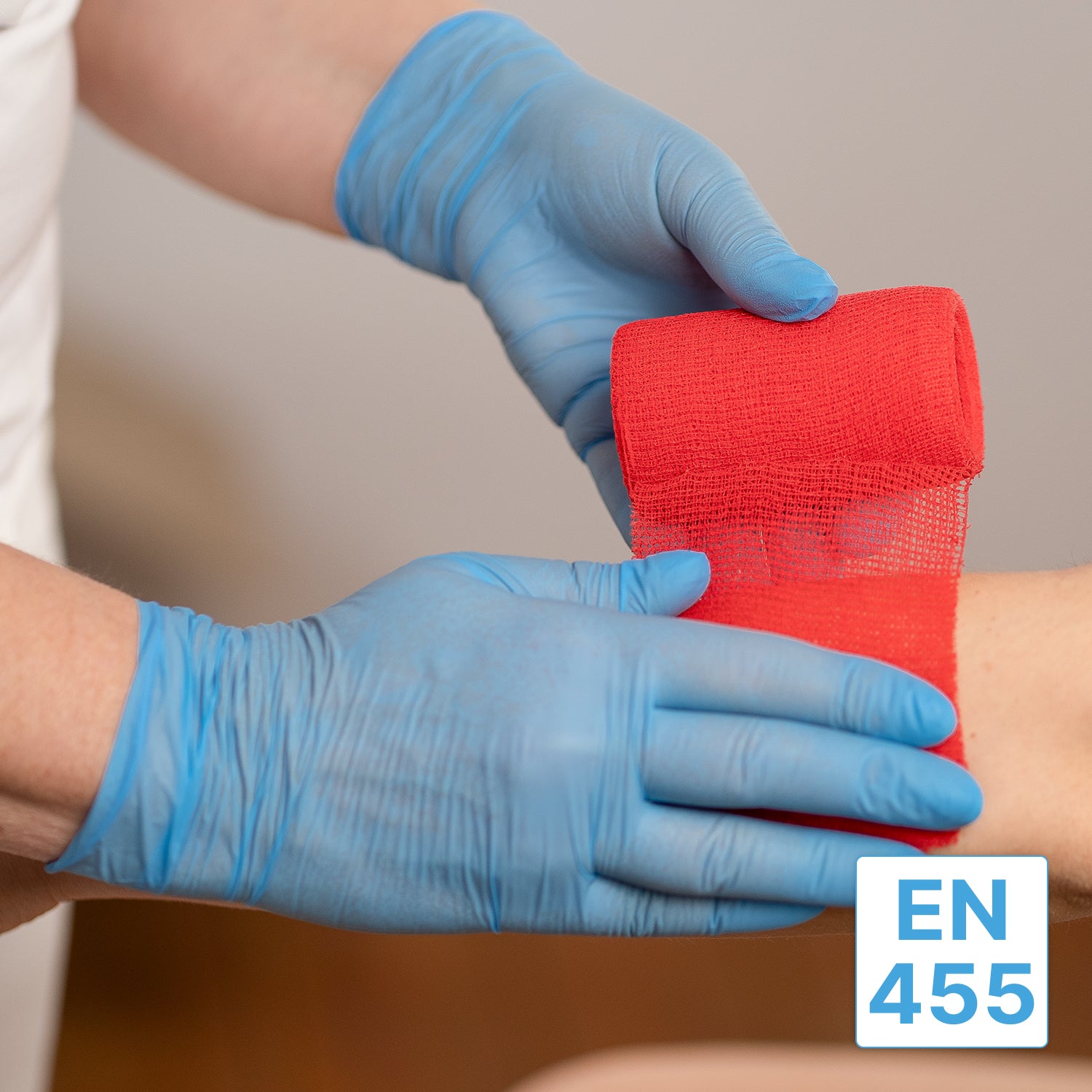 A person wearing ARNOMED NITRIL BLUE 200 nitrile gloves blue from ARNOWA GmbH wraps a red bandage around a person's forearm. A small blue and white label with the inscription "EN 455" appears in the lower right corner of the image.