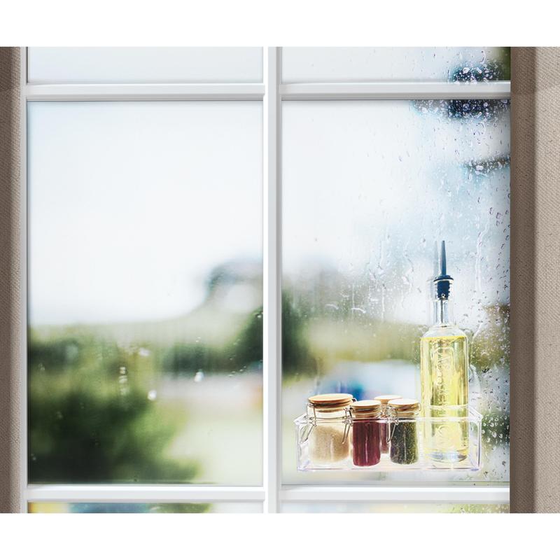 A window with raindrops shows an outdoor scene. On the windowsill, there is a bottle of oil, three small jars with golden lids, and a roll of Scotch-FIX™ Transparent Double-Sided Mounting Tape 4910C from 3M Deutschland GmbH.