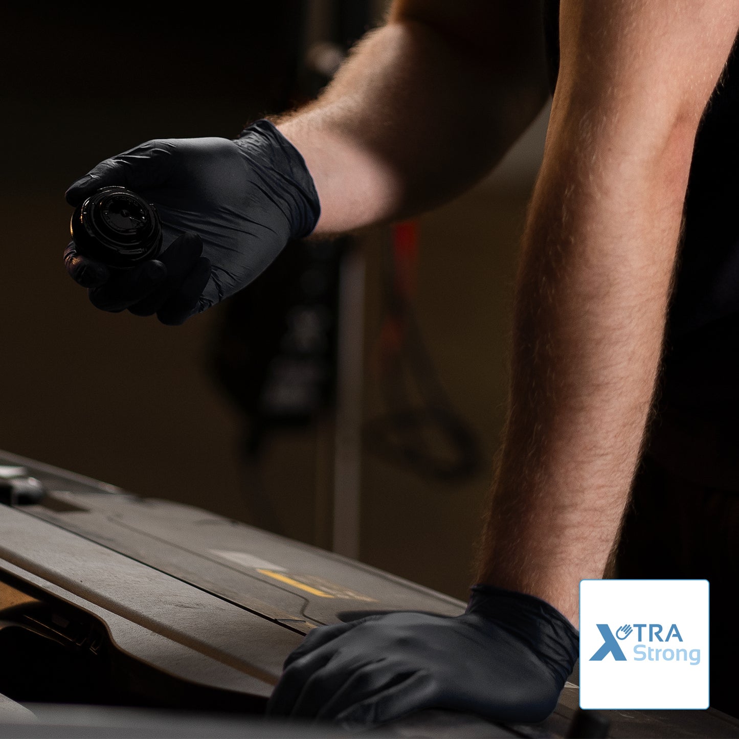 A person wearing ARNOMED NITRIL BLACK XTRA STRONG disposable gloves made of nitrile from ARNOWA GmbH in black works on a car. The "XTRA Strong" logo is visible in the image.
