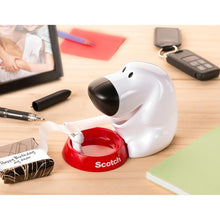 The Scotch™ desktop dispenser in dog design C31 with Scotch® Magic™ invisible tape (19 mm x 8.89 m, 1 roll/package) by 3M Deutschland GmbH sits on the desk between office supplies like a notebook and marker.
