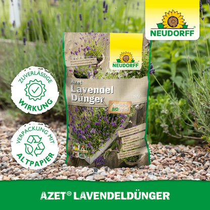 A bag of Neudorff Shop Azet Lavender Fertilizer lies on a gravel garden path next to lavender with blue-violet flowers. The packaging reads "environmentally friendly" in German.