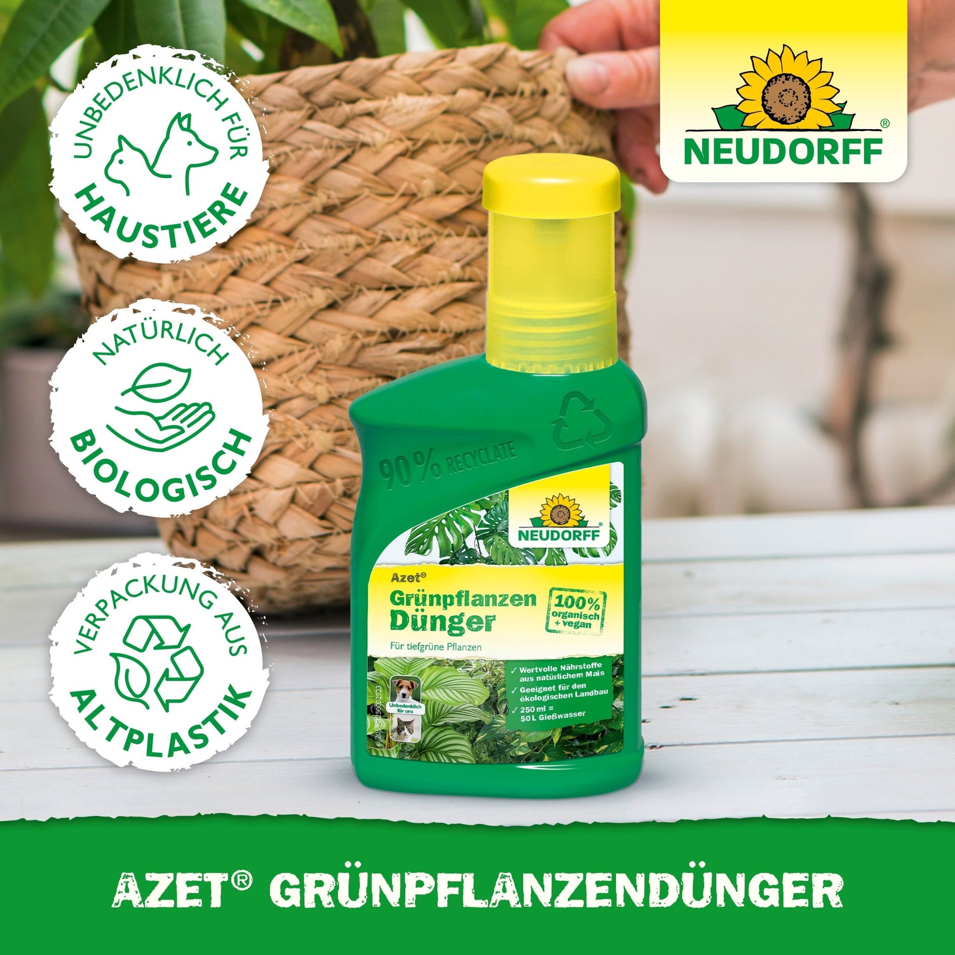 A green bottle of Neudorff Shop Azet Green Plant Fertilizer liquid stands on a table next to a potted plant. The label lists nutrients for green plants, pet safety, natural ingredients, and recycled packaging. A hand is visible in the background.